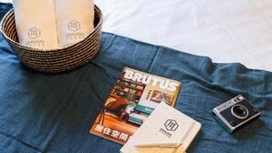 A bed with a blue blanket, a magazine titled 'BRUTUS', a camera, and a basket with towels. - Chuan House Kuromon (Osaka)