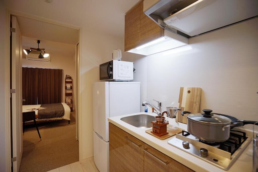 Une cuisine compacte équipée d’un four à micro-ondes, d’un évier, d’une cuisinière et d’un petit coin repas, avec un lit en arrière-plan.
