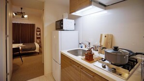A compact kitchen with a microwave, sink, stove, and a small dining area with a bed in the background. - Chuan House Kuromon (Osaka)