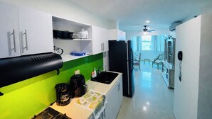 Una cocina moderna con armarios blancos, un refrigerador negro y un salpicadero verde. Hay una cafetera y un hervidor en la encimera.