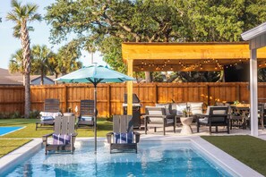 A backyard with a swimming pool, lounge chairs, a barbecue area, and a wooden fence. - Heated Pool | Pickleball | Golf Cart | Putting (Jacksonville Beach)