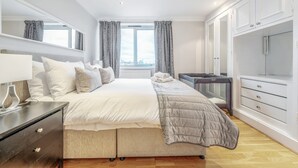 A bedroom with a large bed, a dresser, a mirror, a window with curtains, and a wardrobe. - Stunning Flat in Chelsea Kings Road With Balcony (London)