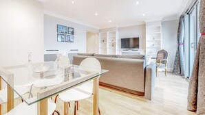 A modern living room with a glass dining table, a sofa, and a TV. - Stunning Flat in Chelsea Kings Road With Balcony (London)