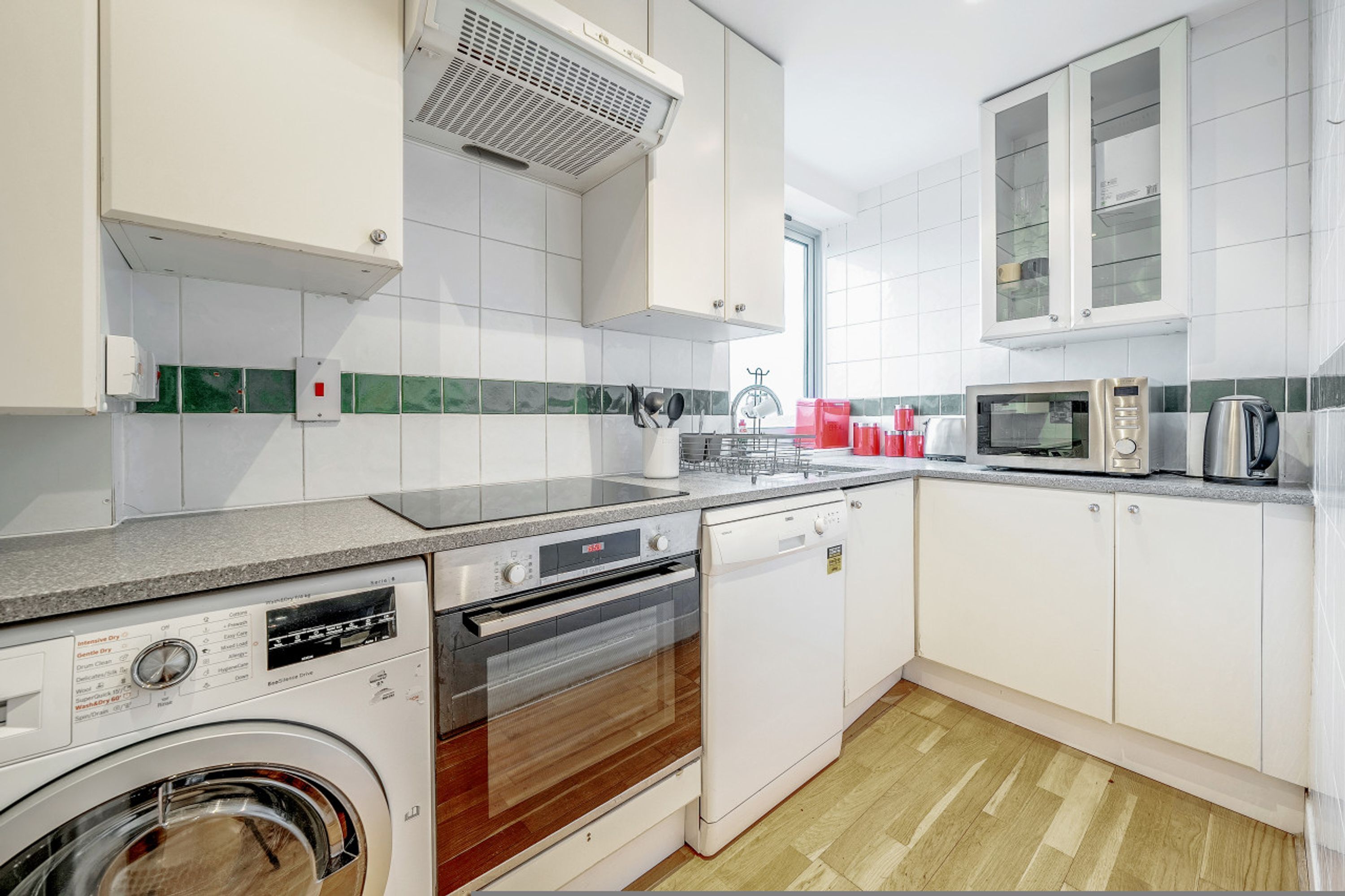 A modern kitchen with white cabinets, a built-in oven, a dishwasher, and a washing machine.
