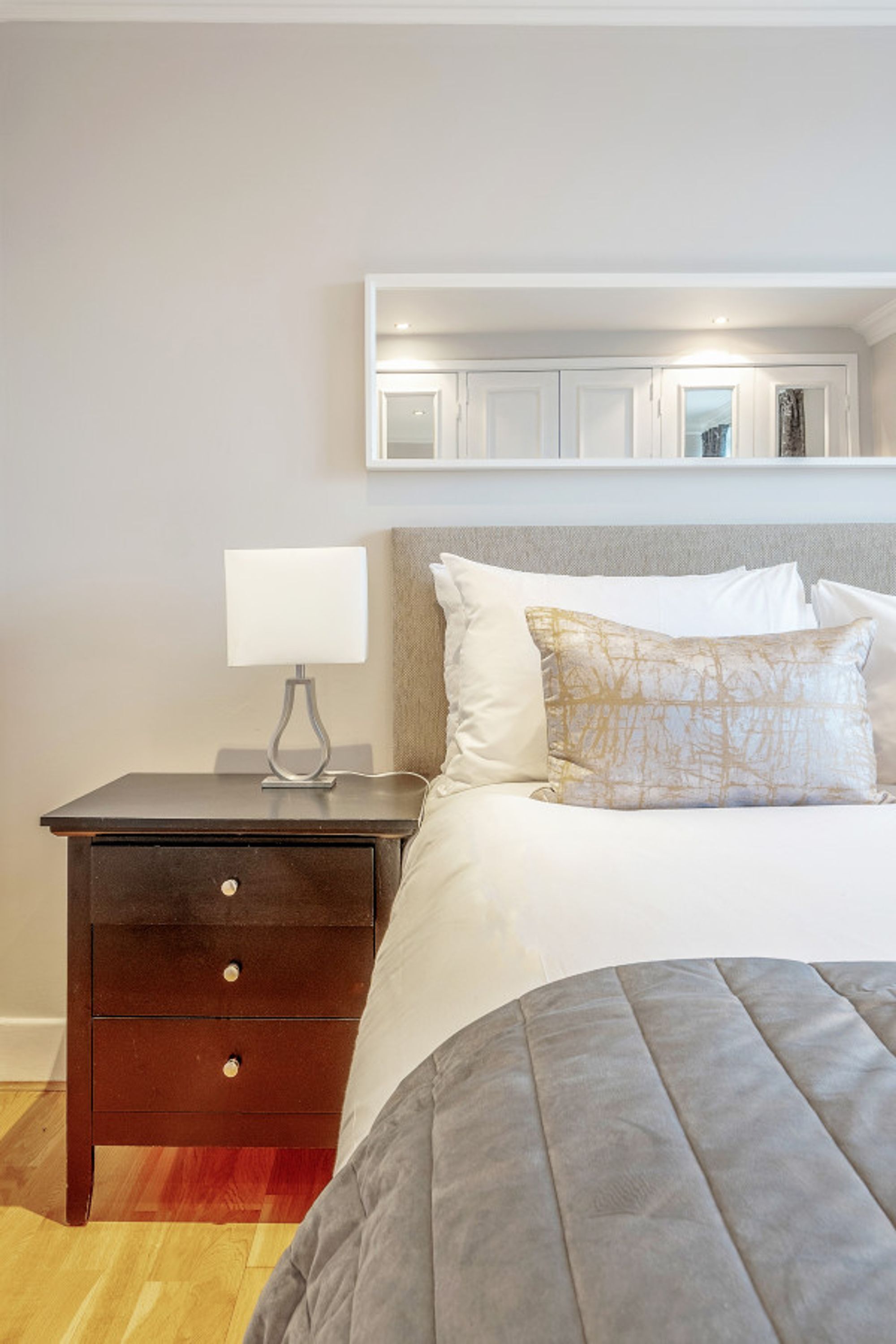 A bedroom with a bed, a nightstand, a lamp, and a wall-mounted shelf above the bed.