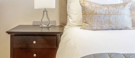 A bedroom with a bed, a nightstand, a lamp, and a wall-mounted shelf above the bed.
