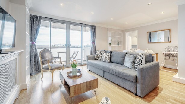 A modern living room with a grey sofa, a wooden coffee table, and a large window with curtains. - Stunning Flat in Chelsea Kings Road With Balcony (London)