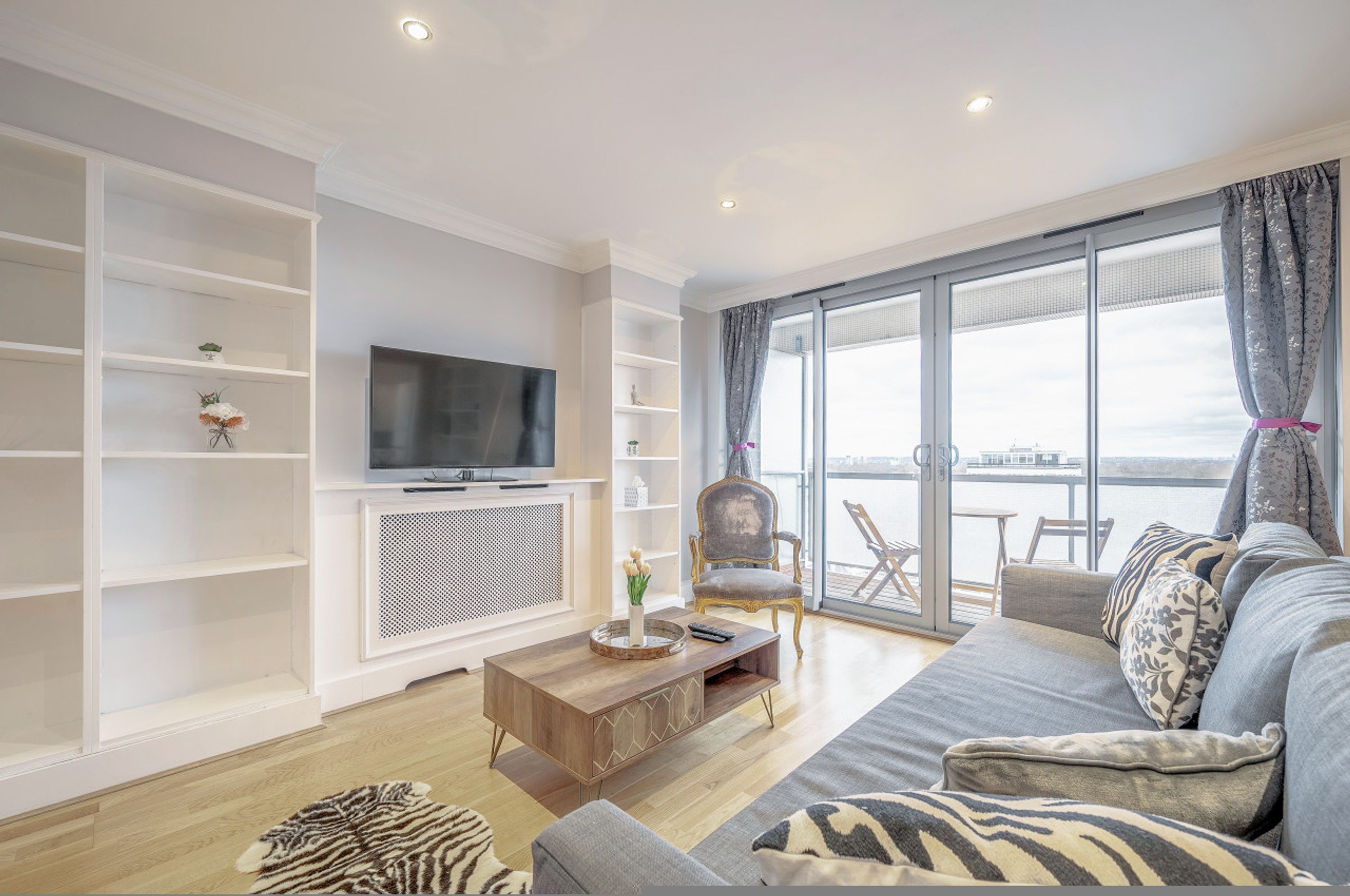 Een moderne woonkamer met een grote flatscreen-tv, een bank, een salontafel en een balkon met uitzicht.