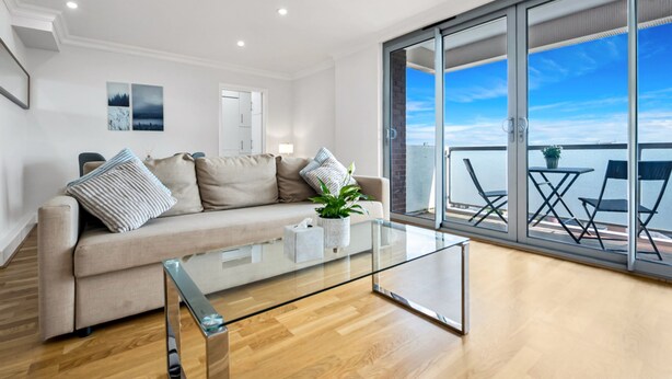 A modern living room with a glass coffee table, a sofa with cushions, a potted plant, and a view of the sea through large sliding glass doors. - Stunning Flat in Chelsea Kings Road With Balcony (London)