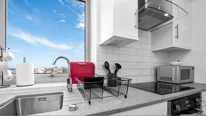 A modern kitchen with a stainless steel sink, a red appliance, a microwave, and a view of the city. - Stunning Flat in Chelsea Kings Road With Balcony (London)