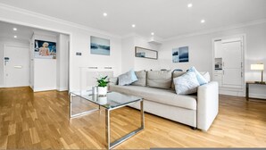 A modern living room with a glass coffee table, a beige sofa with cushions, and a painting on the wall. - Stunning Flat in Chelsea Kings Road With Balcony (London)