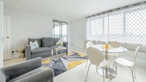 A modern living room with a grey sofa, a glass coffee table, and a round dining table with white chairs. - Stunning Flat in Chelsea Kings Road With Balcony (London)
