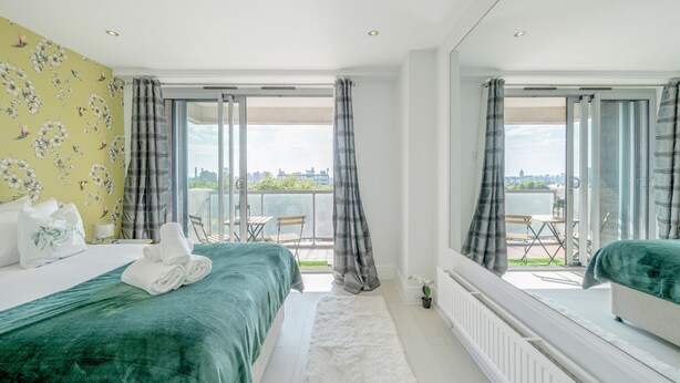 A hotel room with a bed, a view of the city, and a balcony with a table and chairs. - Stunning Flat in Chelsea Kings Road With Balcony (London)