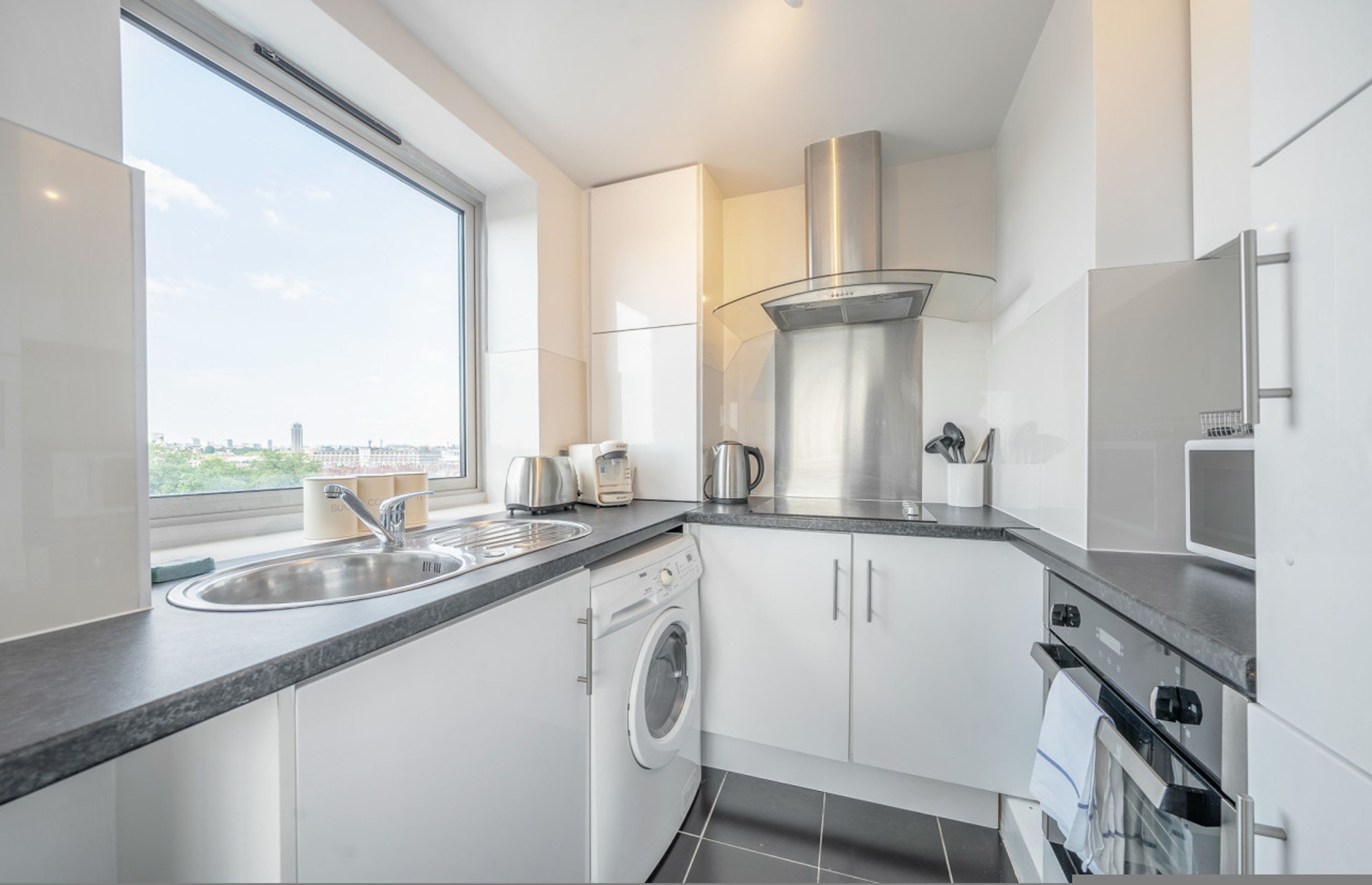 A modern kitchen with a built-in washer, stainless steel appliances, and a large window offering a city view.