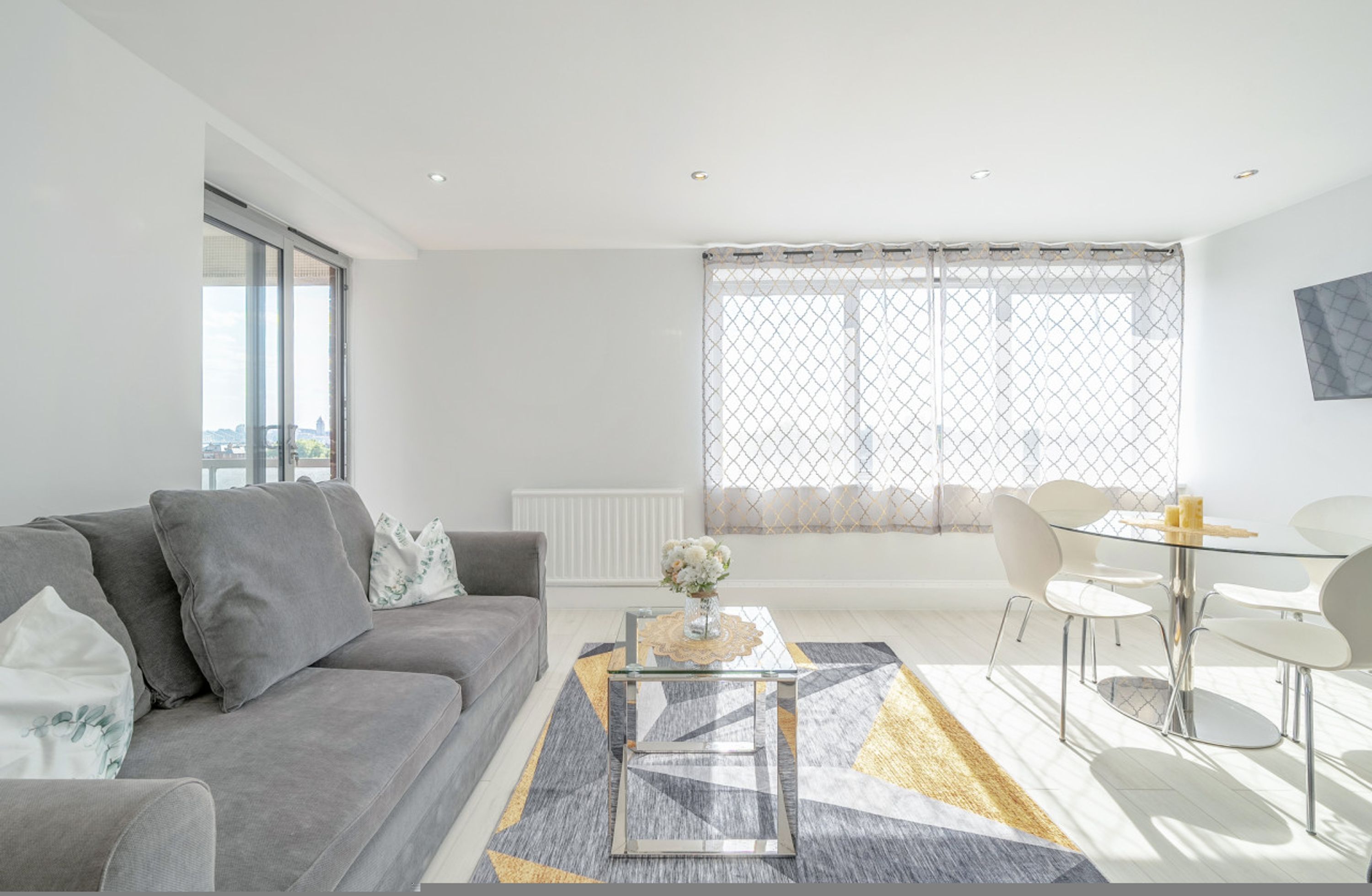 Un salon moderne avec un canapé gris, une table basse en verre et un coin repas avec des chaises blanches.