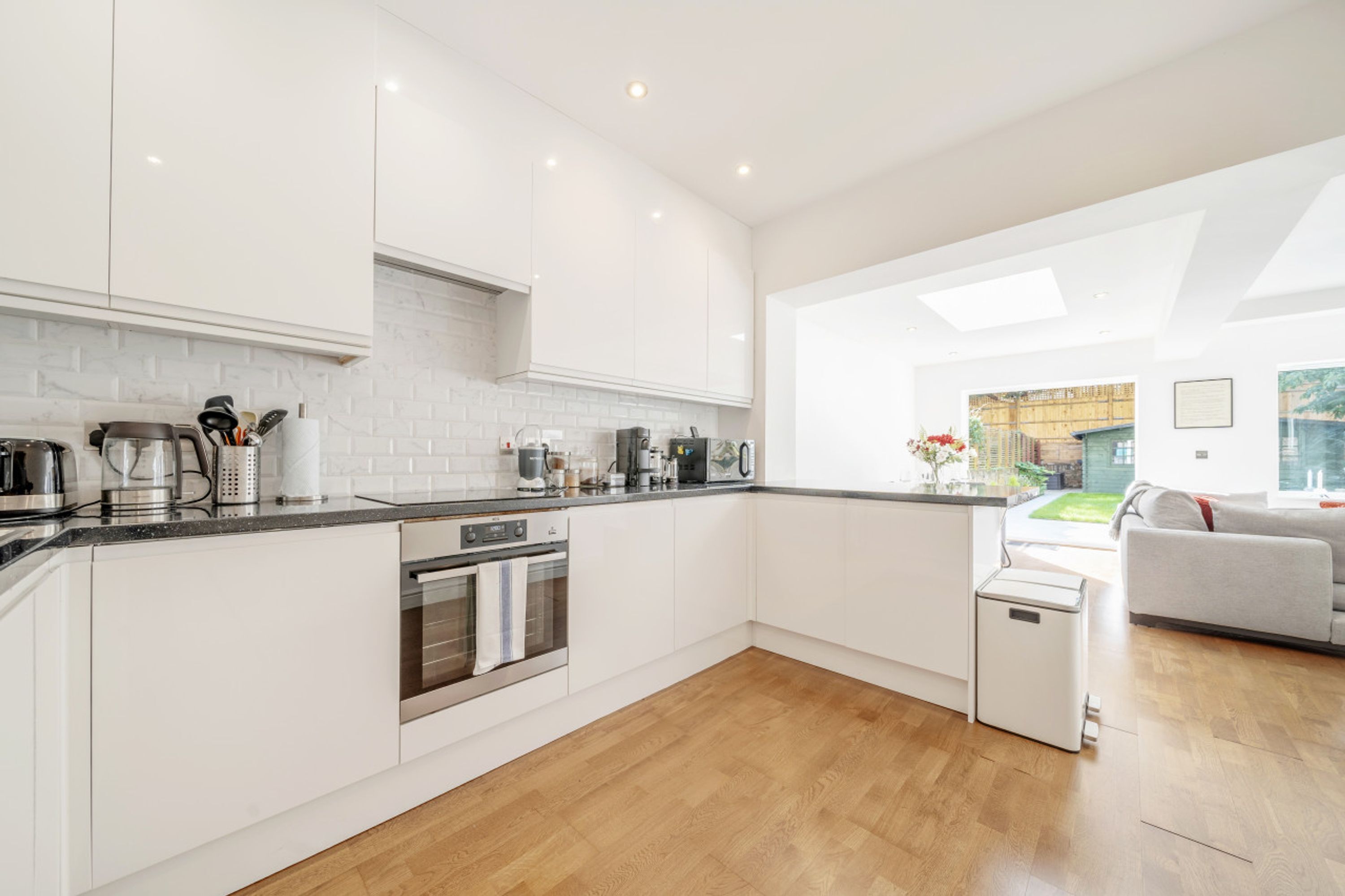 A modern kitchen with white cabinetry, a built-in oven, and a coffee machine.
