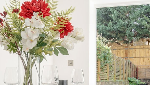 A dining table set for four with a vase of red and white flowers, two wine glasses, and a black chair in the foreground. - Maida Vale Gem by Little Venice (London)
