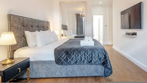 A modern hotel room with a large bed, a bedside table with a lamp, a flat-screen TV mounted on the wall, and a mirror reflecting the room. - Maida Vale Gem by Little Venice (London)