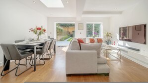 A modern living room with a dining area, large windows, and a flat-screen TV. - Maida Vale Gem by Little Venice (London)