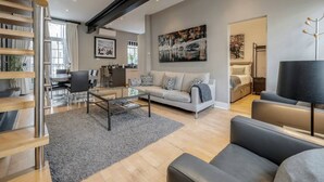 A modern living room with a sofa, coffee table, and a staircase. - Conduit Mews Luxurious Mews House Next to Hyde Park (London)