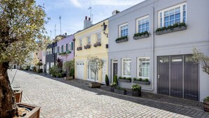 A cobblestone street lined with colorful buildings, each with windows and planters. - Conduit Mews Luxurious Mews House Next to Hyde Park (London)