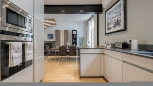 A modern kitchen with built-in appliances, a dining area with chairs, and a large window providing natural light. - Conduit Mews Luxurious Mews House Next to Hyde Park (London)