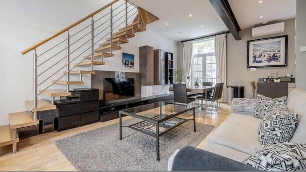 A modern living room with a glass coffee table, a sofa, a staircase, and a kitchen area. - Conduit Mews Luxurious Mews House Next to Hyde Park (London)