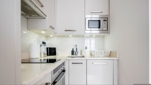 Una cocina moderna con armarios blancos, microondas integrado, cafetera y lavamanos.