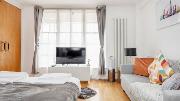 Un dormitorio moderno con cama, televisor, sofá y ventana con cortinas.