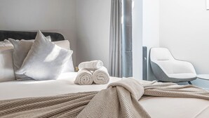 Hotellihuone, jossa on sänky, tyynyjä, tuoli ja näkymä ulos.