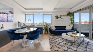 A modern living room with a dining area, large windows, and a city view. - Stunning Flat in Chelsea Kings Road With Balcony (London)