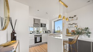 A modern kitchen with white cabinetry, a central island, bar stools, and pendant lighting. - Stunning Flat in Chelsea Kings Road With Balcony (London)