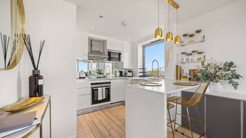 A modern kitchen with white cabinetry, a central island, bar stools, and pendant lighting.