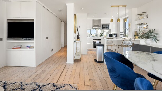 A modern kitchen with white cabinets, a built-in oven, and a dining area with a marble table and blue chairs. - Stunning Flat in Chelsea Kings Road With Balcony (London)