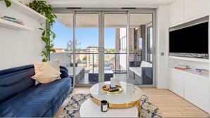 A modern living room with a dark blue sofa, a round coffee table, and a TV mounted on the wall. - Stunning Flat in Chelsea Kings Road With Balcony (London)