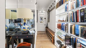 A well-lit hallway with a wooden bench, a bookshelf filled with books, and decorative vases on a table. - Stunning Flat in Chelsea Kings Road With Balcony (London)