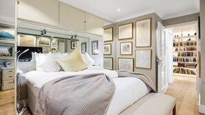 A bedroom with a large bed, bedside tables, a wardrobe, and a bookshelf filled with books. - Stunning Flat in Chelsea Kings Road With Balcony (London)