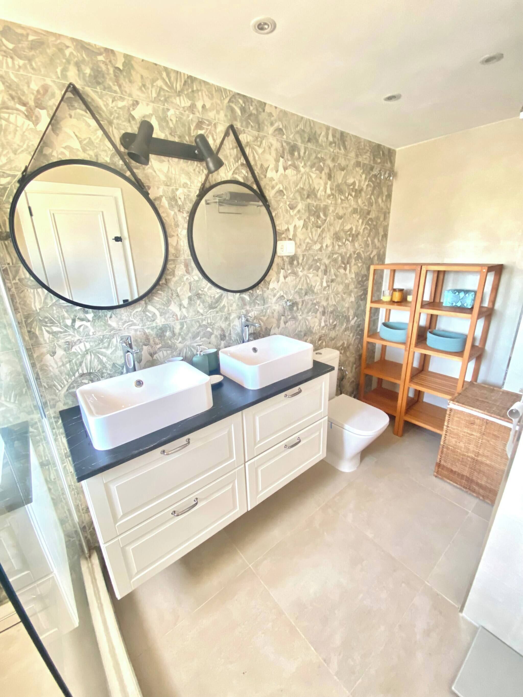 Une salle de bain avec deux lavabos, un miroir et une étagère en bois.
