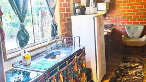 A compact kitchen with a sink, stove, and refrigerator, a window with curtains, and a rustic wooden ceiling. - Tarumã Challes 04, Complete chalet with balcony and barbecue, pets allowed. (Bonito)