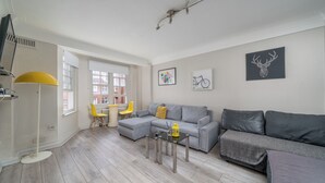A modern living room with a grey sectional sofa, a yellow chair, a small table, and artwork on the walls. - 1 Bed Flat in London (London)