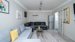 A modern living room with a grey sofa, a black armchair, and a small coffee table. There is a framed picture on the wall and a door with a gold frame leading to another room. - 1 Bed Flat in London (London)