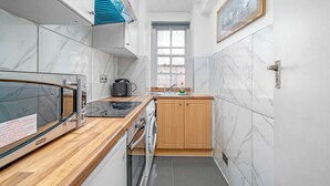 A compact kitchen with marble tiles, wooden cabinets, a built-in oven, and a window. - 1 Bed Flat in London (London)