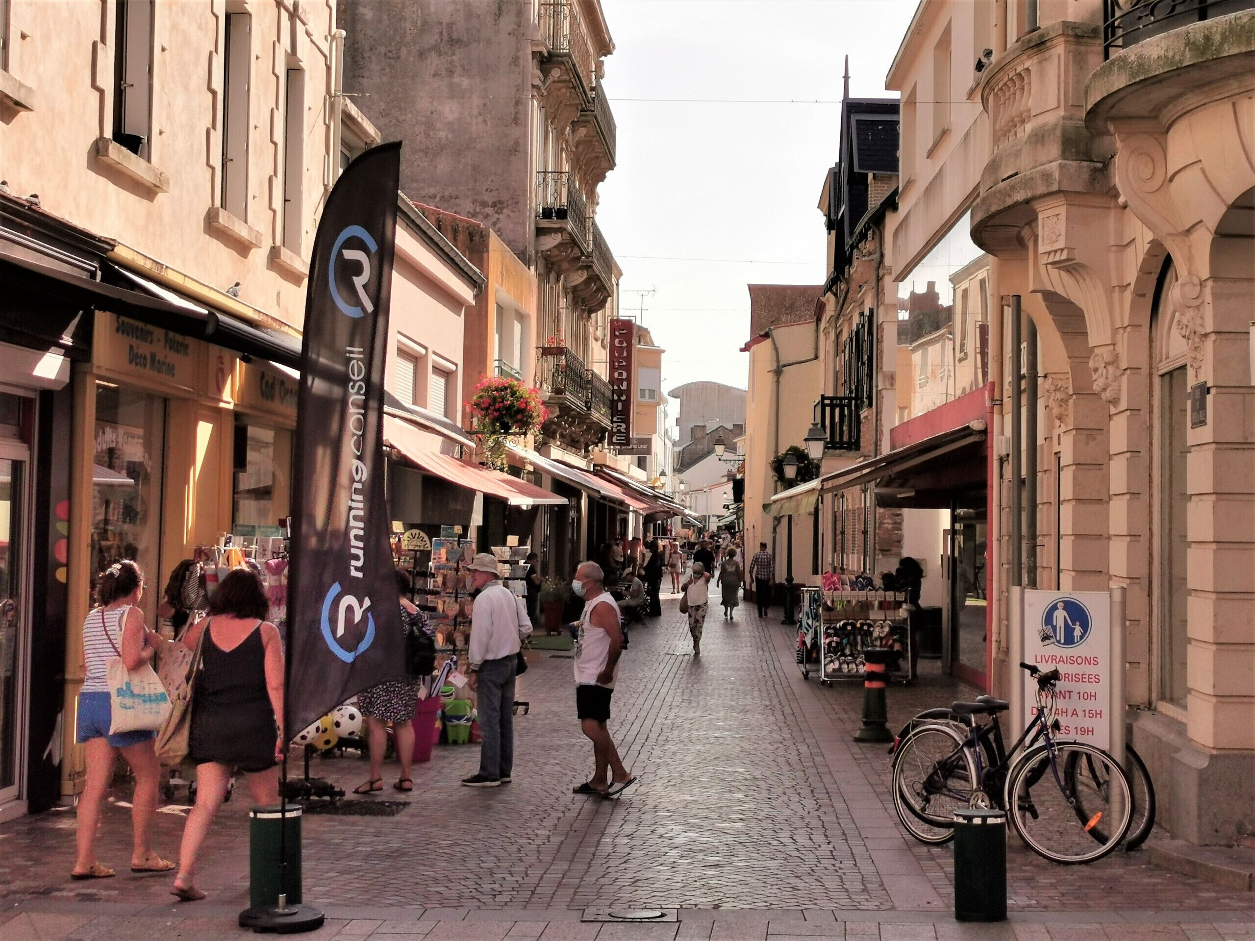 Une rue pavée bordée de boutiques et de cafés, un vélo garé sur le côté et un panneau indiquant une durée maximale de stationnement de 10 heures.