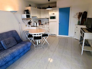 A compact living space with a kitchenette, a dining area with a small table and chairs, a sofa, and a blue door. - CLAIR DE MER - Heated swimming pool (Les Sables-d´Olonne)