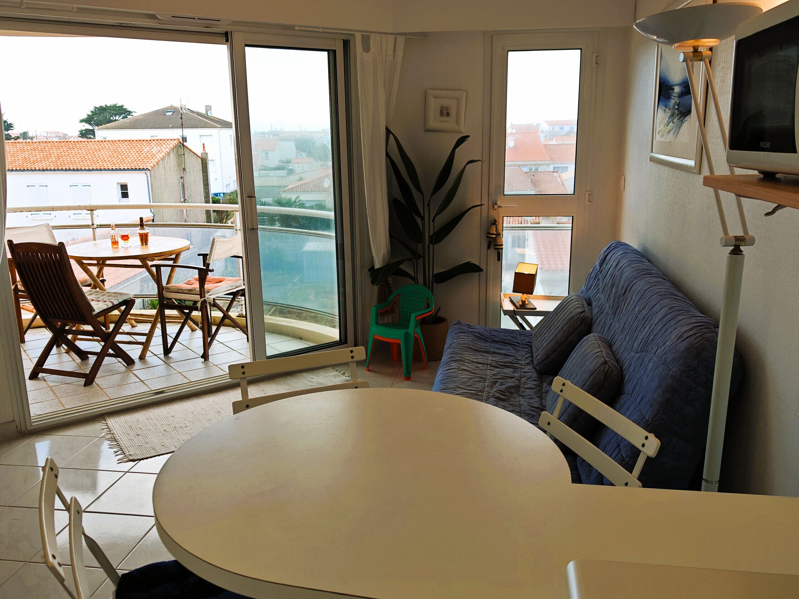 A room with a balcony, a round table, a sofa, and a television.