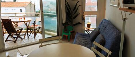 A room with a balcony, a round table, a sofa, and a television.