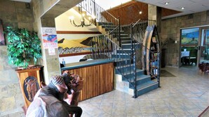 A reception area with a wooden desk, a staircase with metal railings, and a large potted plant.