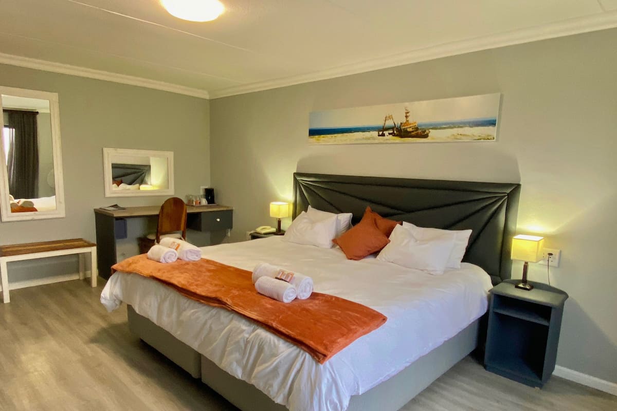 Habitació d'hotel amb un llit gran, una escriptori, una cadira, una tauleta de nit i un quadre a la paret.