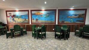 A restaurant with a tiled floor, green upholstered chairs, and three large wall paintings depicting maritime scenes.