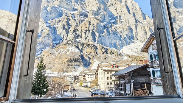 A mountain view through a window, featuring rugged peaks, a town below, and buildings with balconies. - Studio Turmalin by Interhome (Leukerbad)